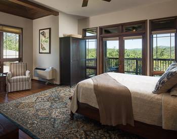 Side angle of the room with Wood platform bed , strip chair in the corner with a blue brown tapestry rug in the middle of the floor